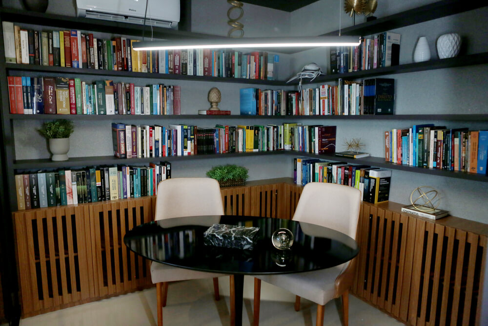Sala do escritório Barbosa Bezerra Lima Advocacia:, com mesa preta redonda, 2 cadeiras brancas e, ao fundo, grande estante com livros