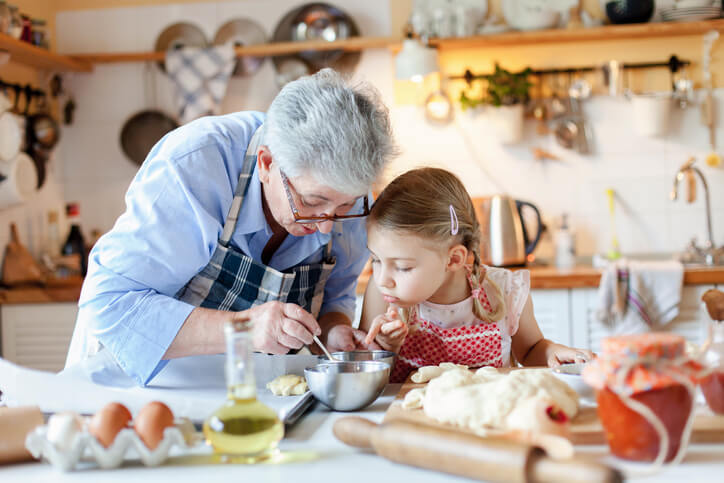 Imagem ilustrativa para o serviço de Planejamento patrimonial e sucessório: avó e neta, uma criança de aproximadamente 6 anos, estão na mesa da cozinha enquanto a avó ensina uma receita